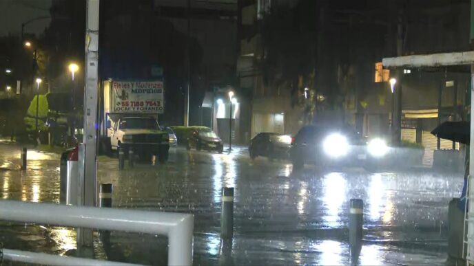 Calle inundada en alcaldía del sur de la Ciudad de México durante temporada de lluvias con vehículos circulando entre el agua